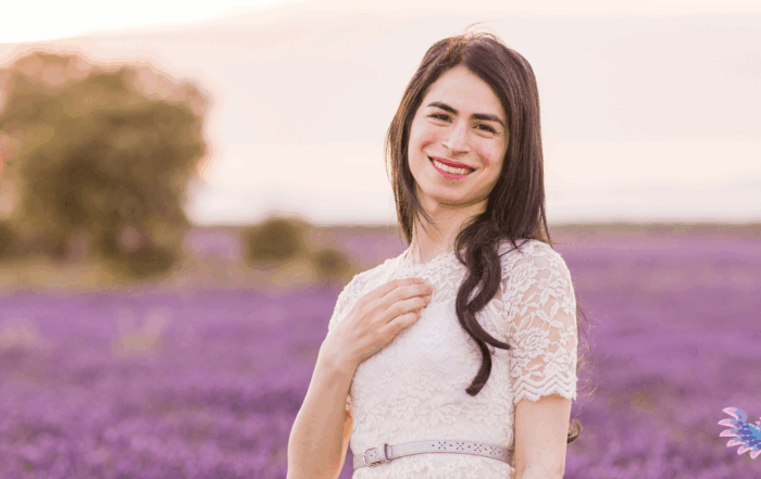 Beautiful transgender person wearing a romantic style dress standing in a field of lavender at sunset smiling beatifically at the viewer