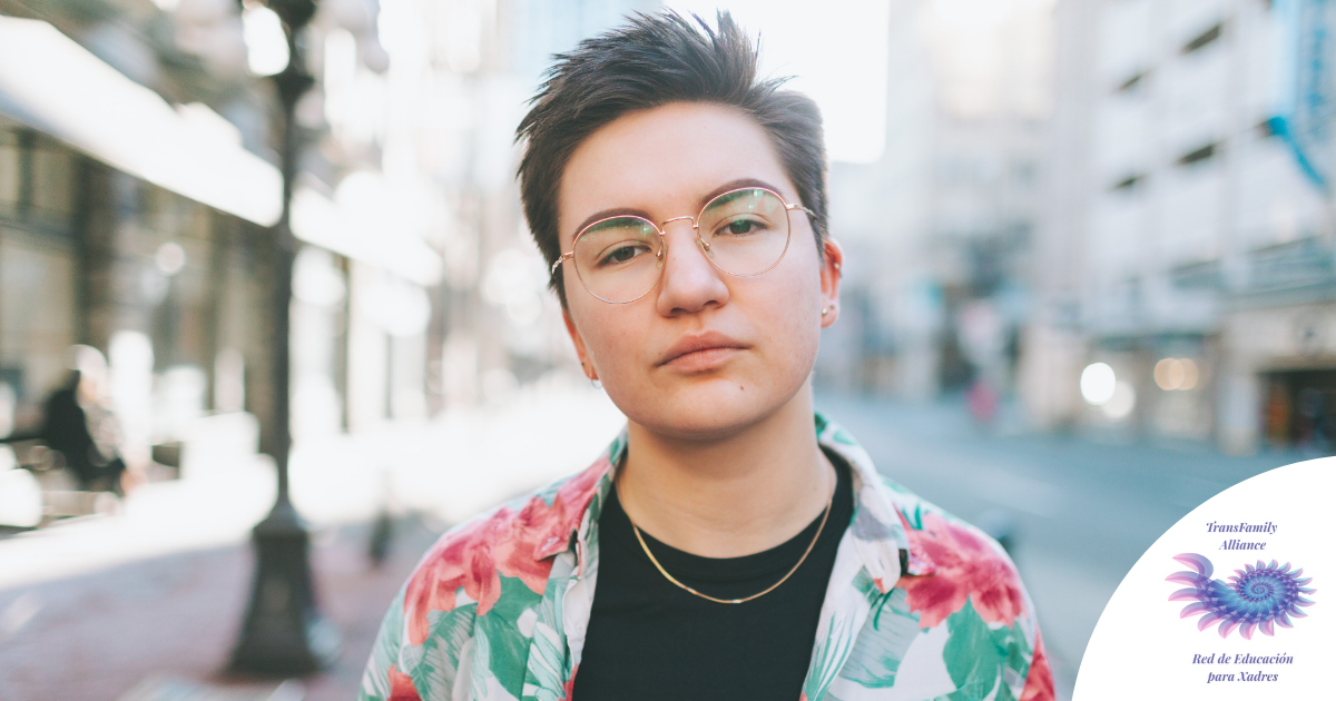 Trans masculine presenting person standing in a city, staring down the camera