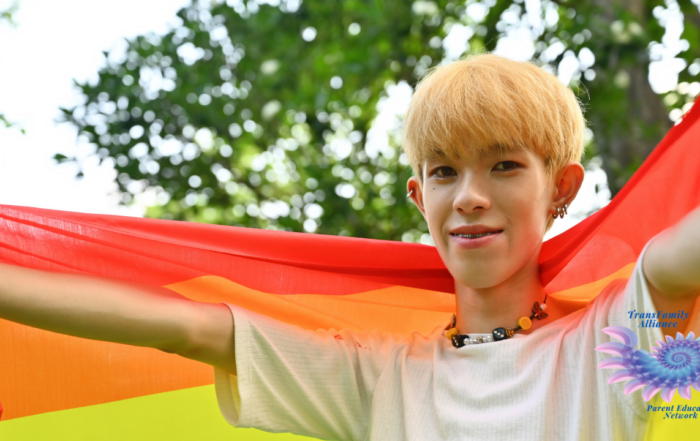 An ambiguous looking young figure draped in a rainbow flag, looking into the camera and evoking the question, Is my kid trans?