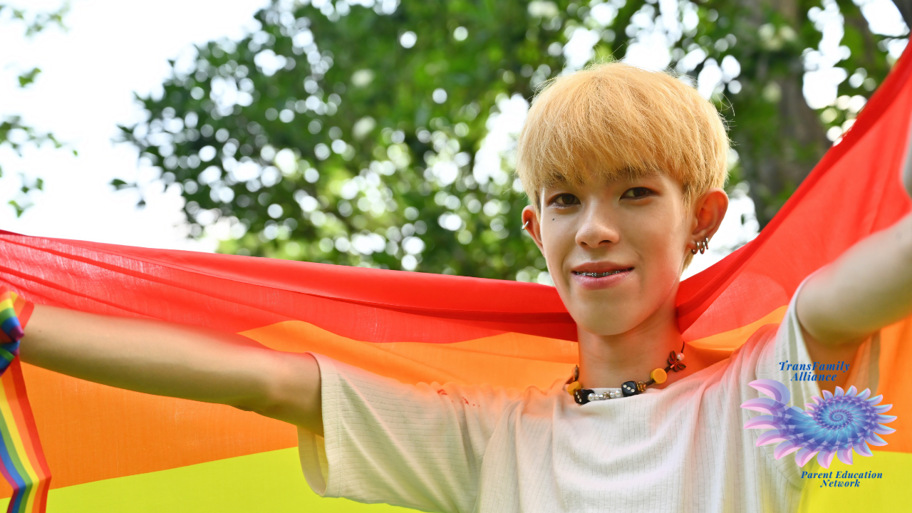 An ambiguous looking young figure draped in a rainbow flag, looking into the camera and evoking the question, Is my kid trans?